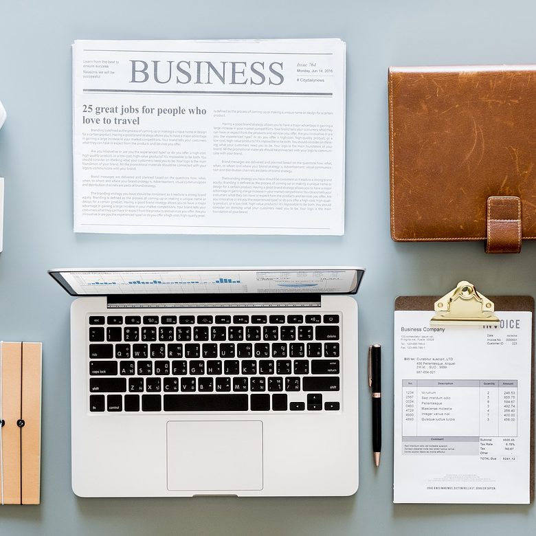 Flatlay of laptop, newspaper, calendar, bilfold, glasses, clipboard and coffee cup - Business Law Eric Everett Hawes